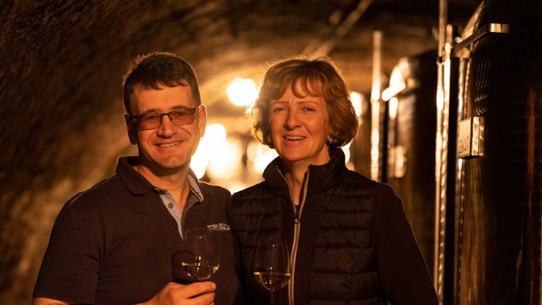 Two people in a wine cellar with wine glasses in their hands.