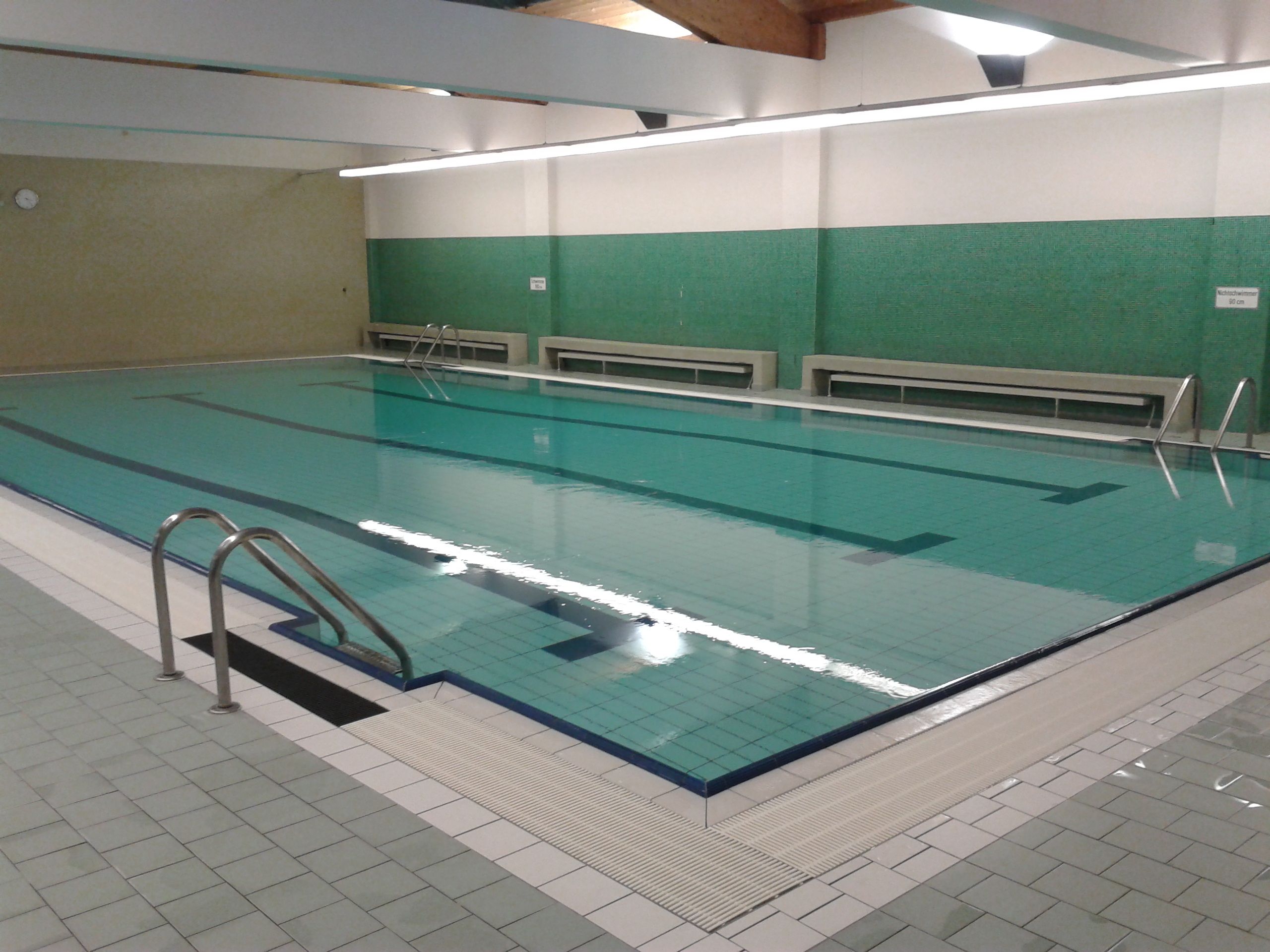 Interior view of an empty indoor pool with green tiled walls and a large swimming pool.