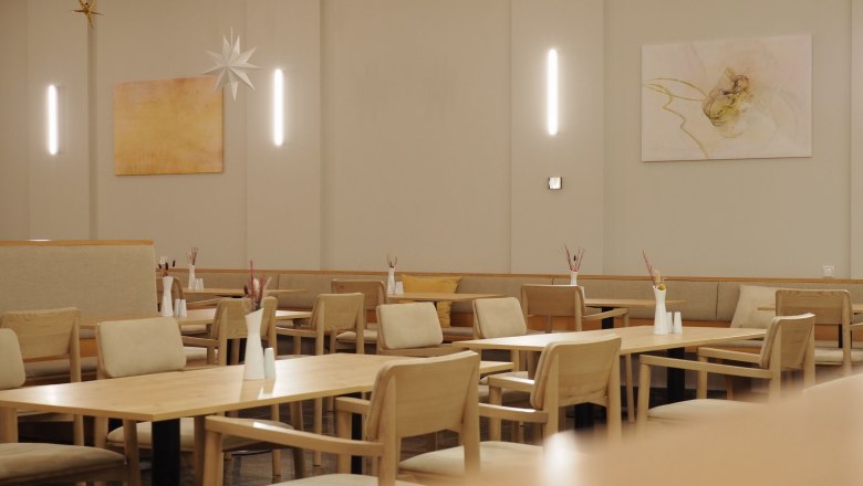 Interior view of a modern restaurant with wooden tables and chairs, decorated with minimalist artwork and star pendants.
