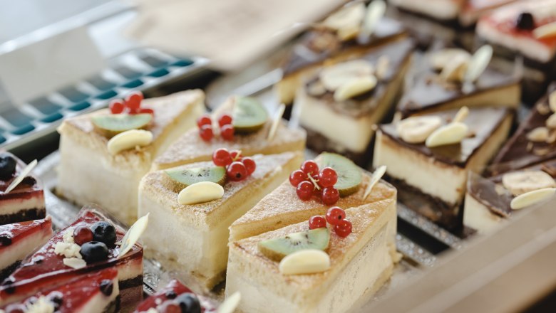 Various pieces of cake in a display case, decorated with fruit and chocolate.