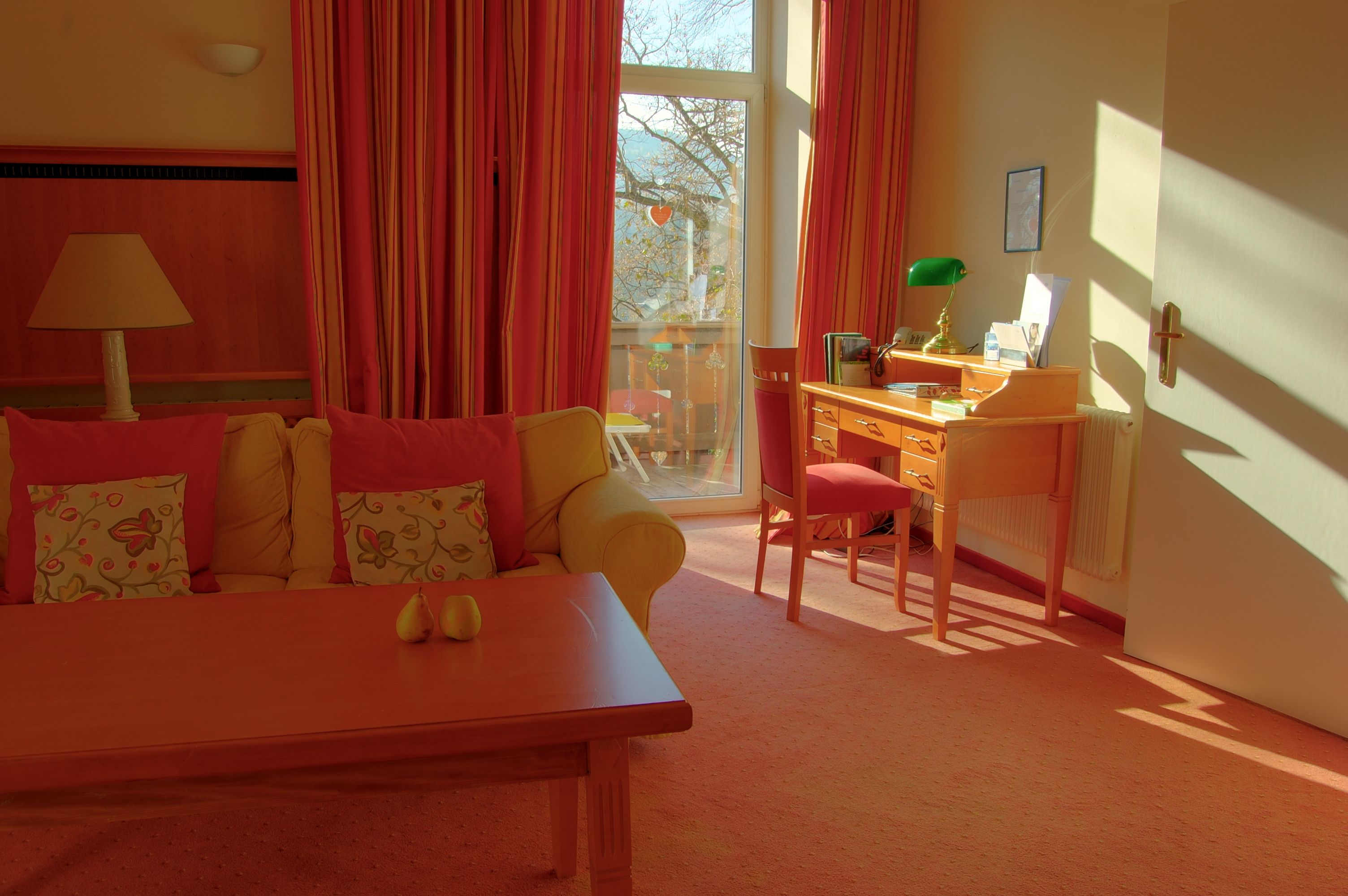 A cozy room with sofa, desk and large window with curtains.