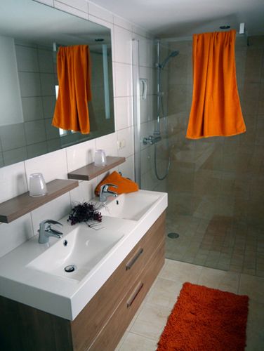 Modern bathroom with double washbasin, large mirror, shower and orange accents.