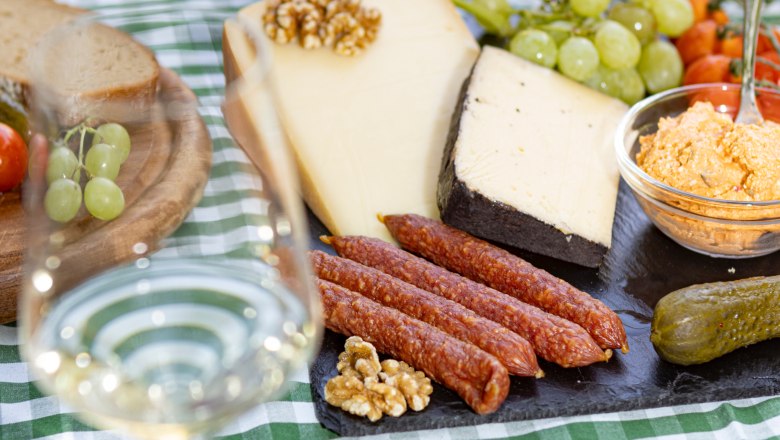 Picnic table with cheese, sausage, bread, grapes and a glass of white wine.