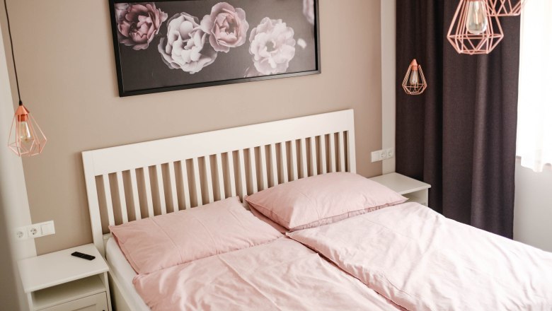 Bedroom with pink bed linen, white bed frame and flower picture on the wall.