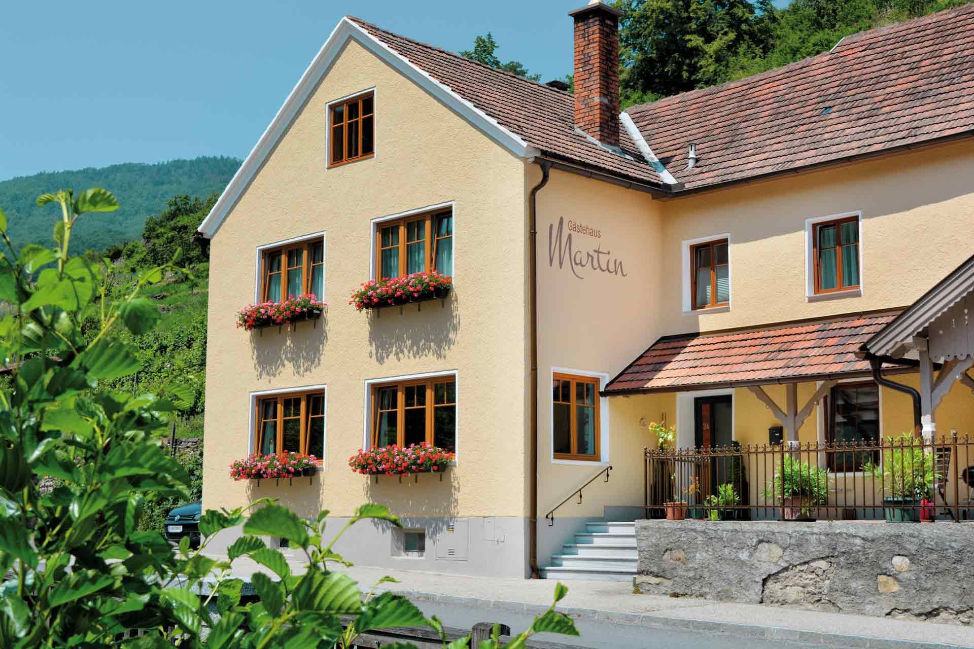 Exterior view of a yellow guest house with red roof tiles and flower boxes on the windows.