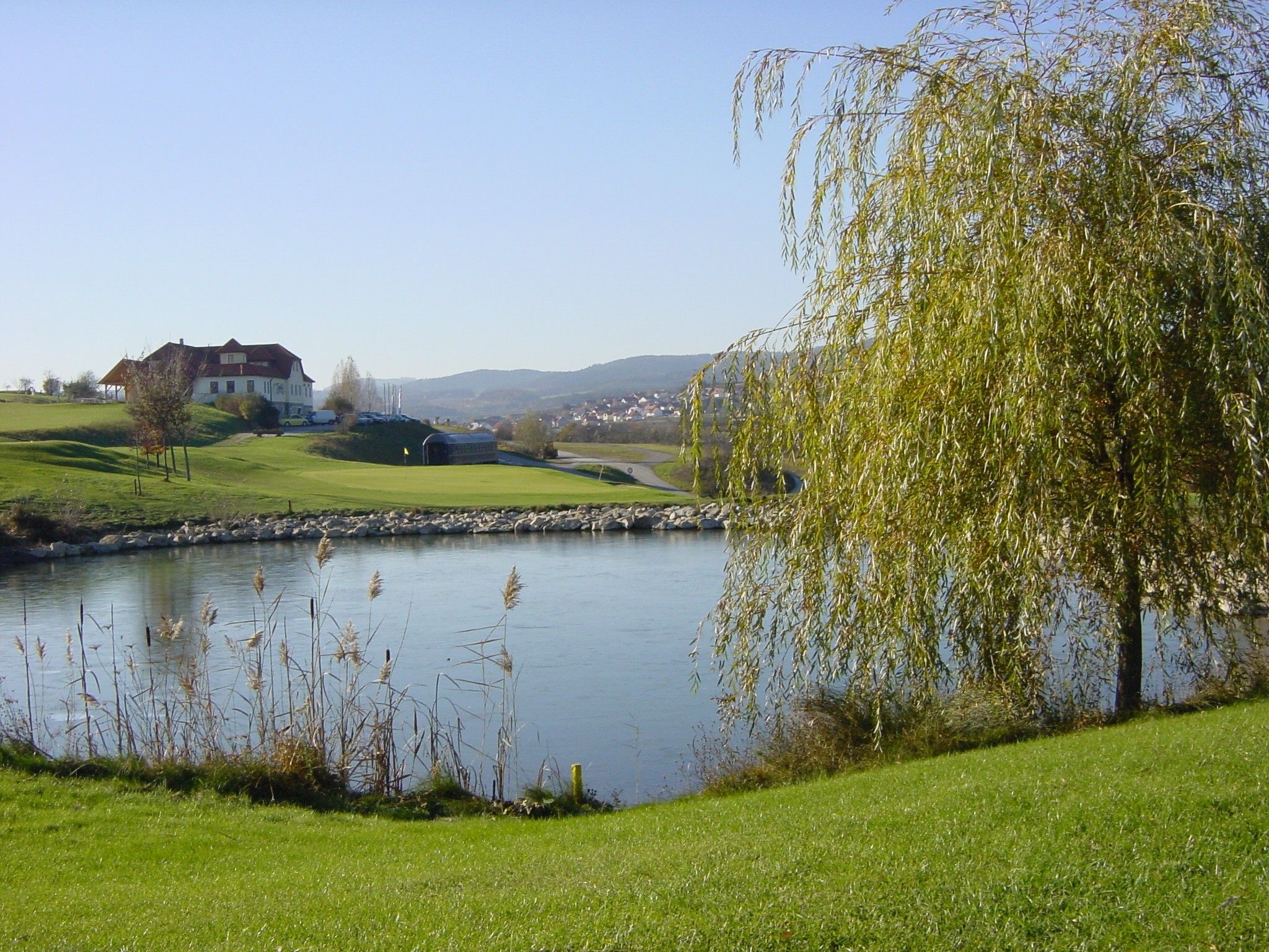 Golf course with pond, trees and a building in the background.