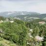 Panoramic view of a mountainous landscape with forest, road and buildings.