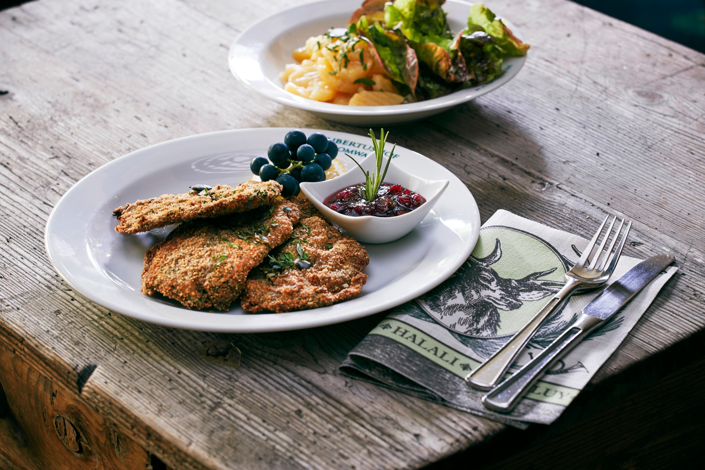 A plate of venison schnitzel, cranberries and grapes on a wooden table.