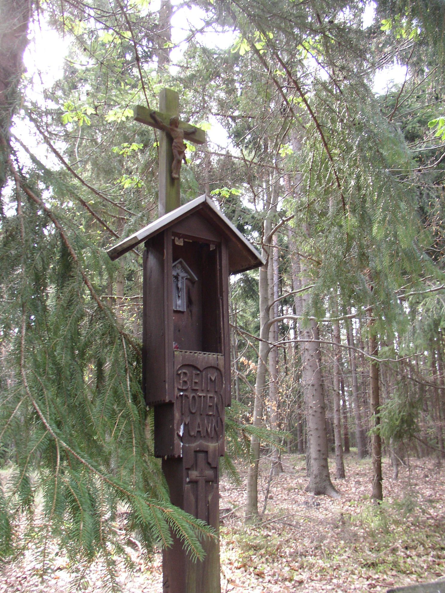Wooden cross with Christ figure in the forest, inscribed with 'Beim Toten Mann'.
