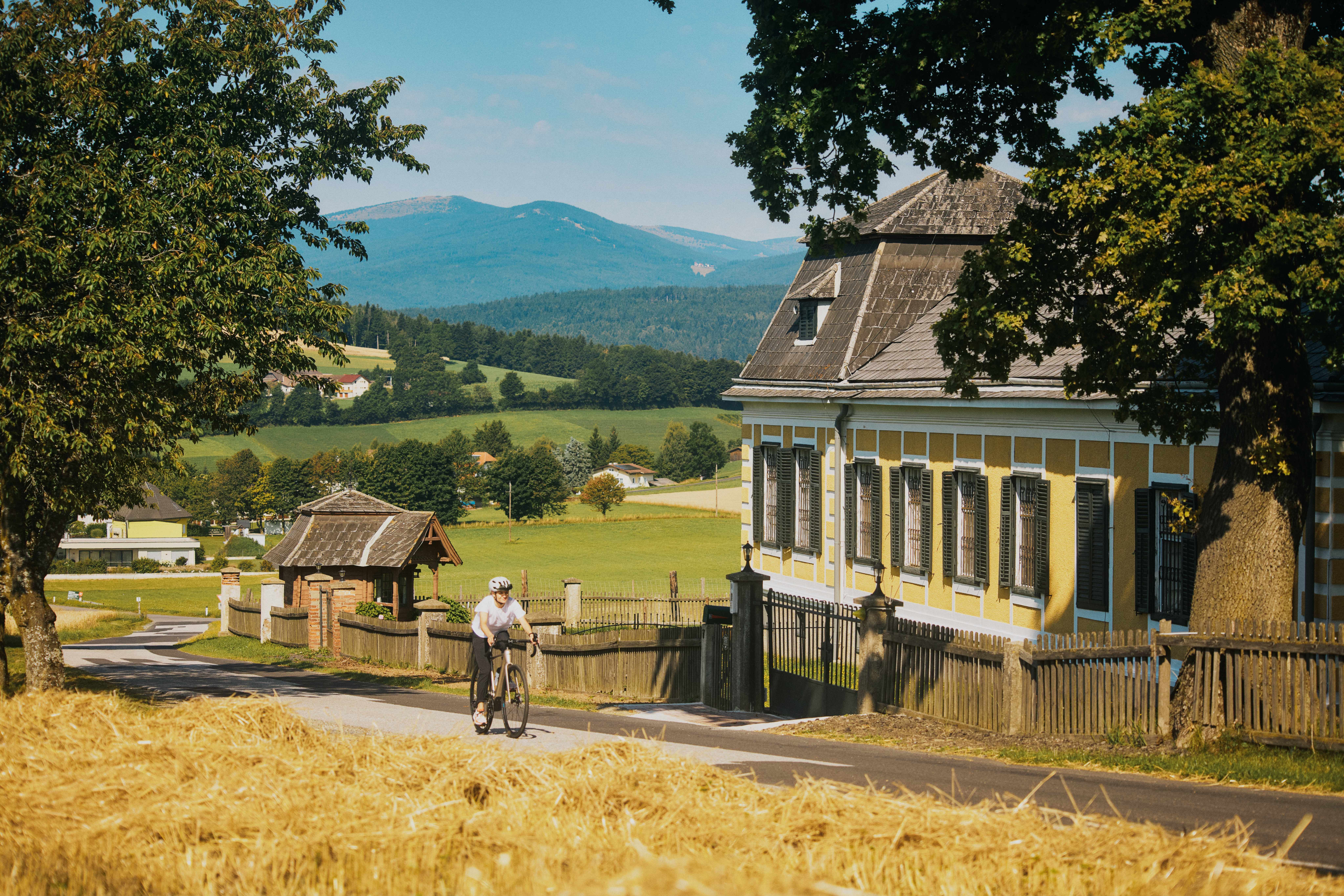 A cyclist on a country road rides past Ziegersberg Castle. The Wechsel in the background.