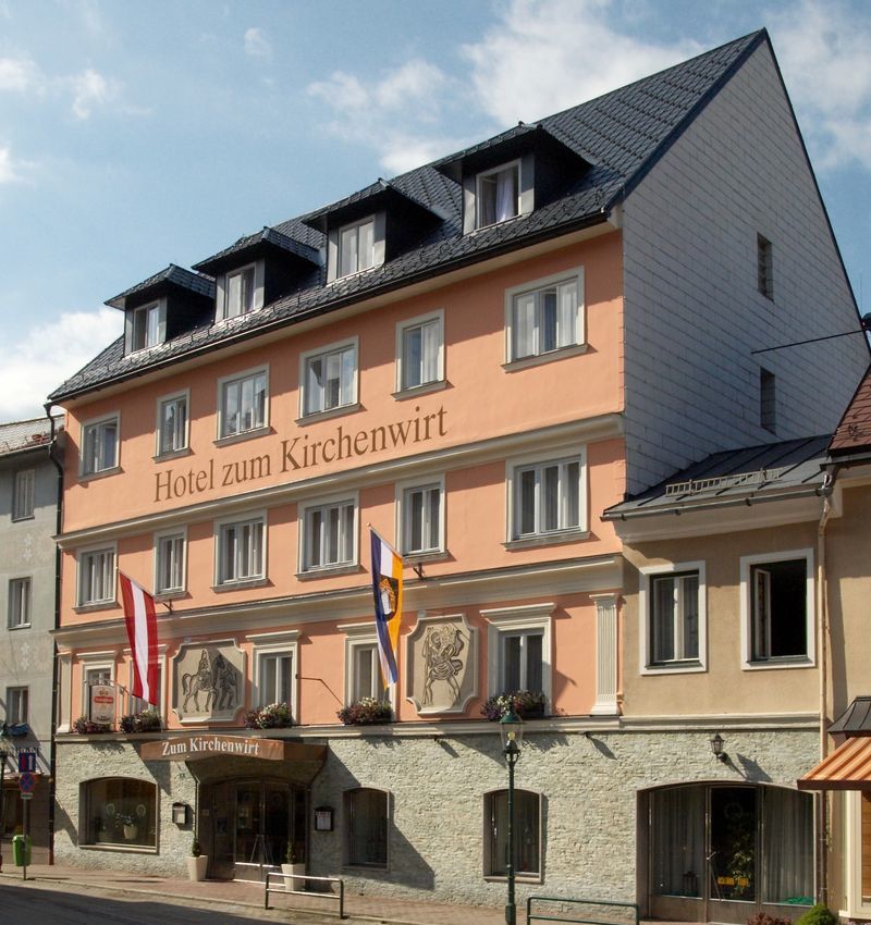 Facade of the Hotel zum Kirchenwirt with flags and blue sky.