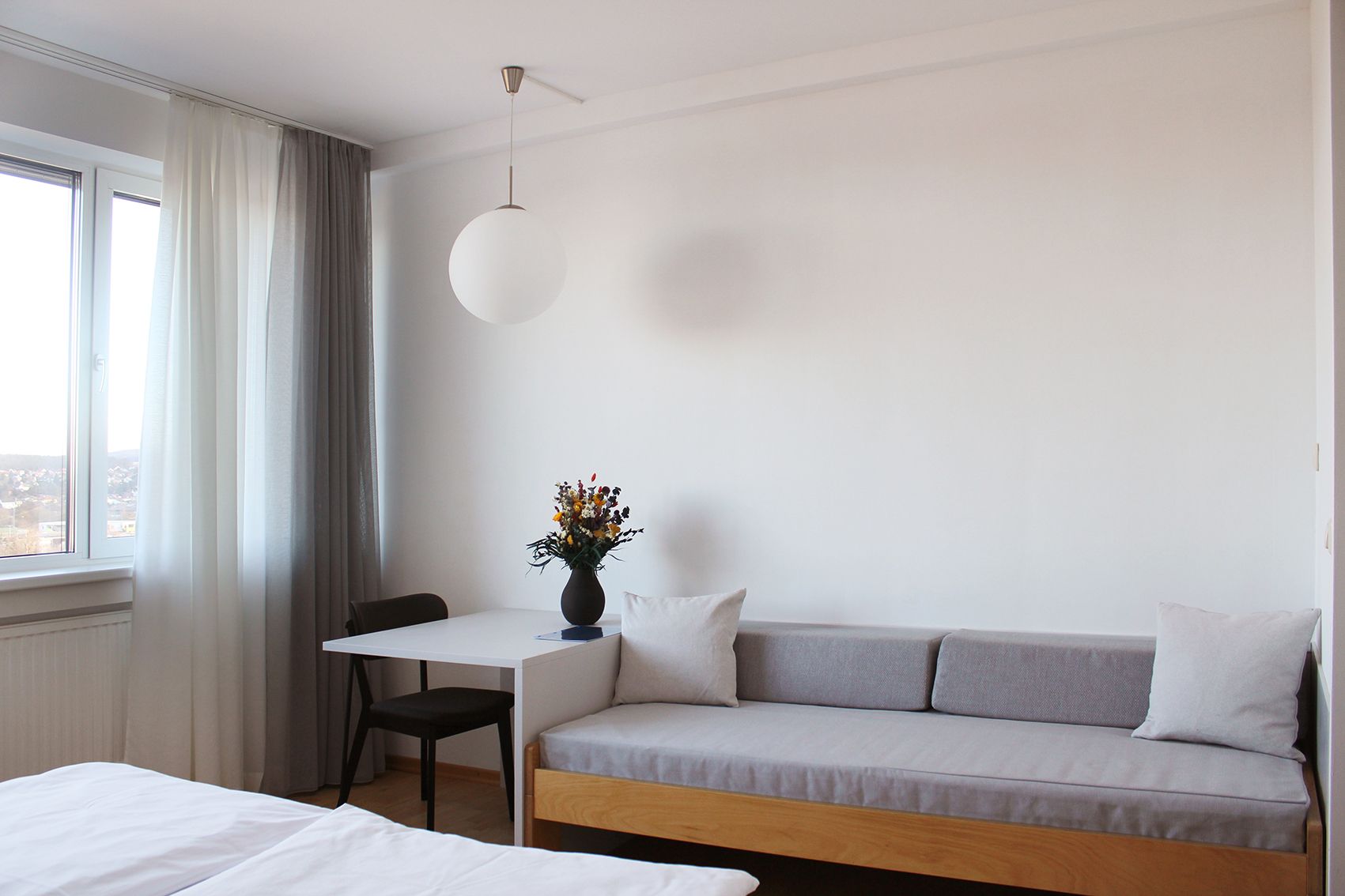 Modern guest room with sofa, table, chair and window with curtains.