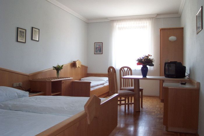 A simply furnished hotel room with two beds, a table, chairs and a small TV.