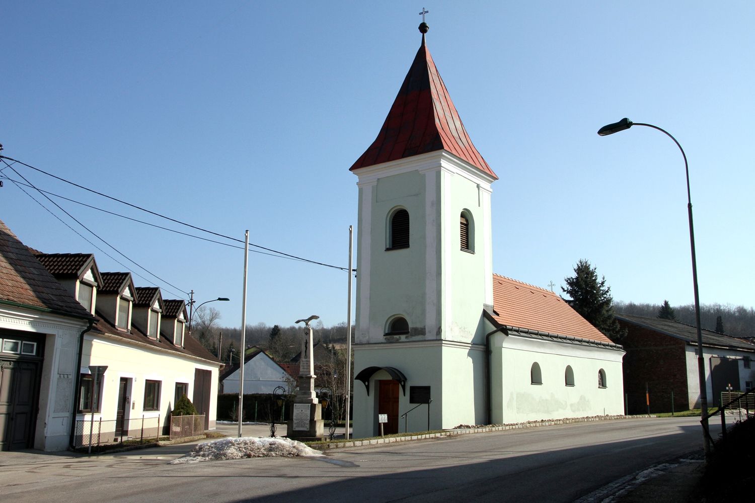 Church with red roof and tower in a village under a clear sky.