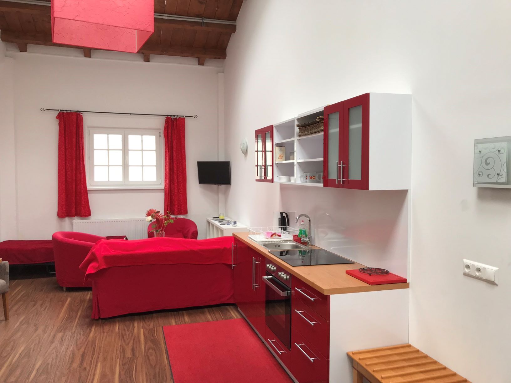 Modern loft kitchen with red accents and wooden floor.