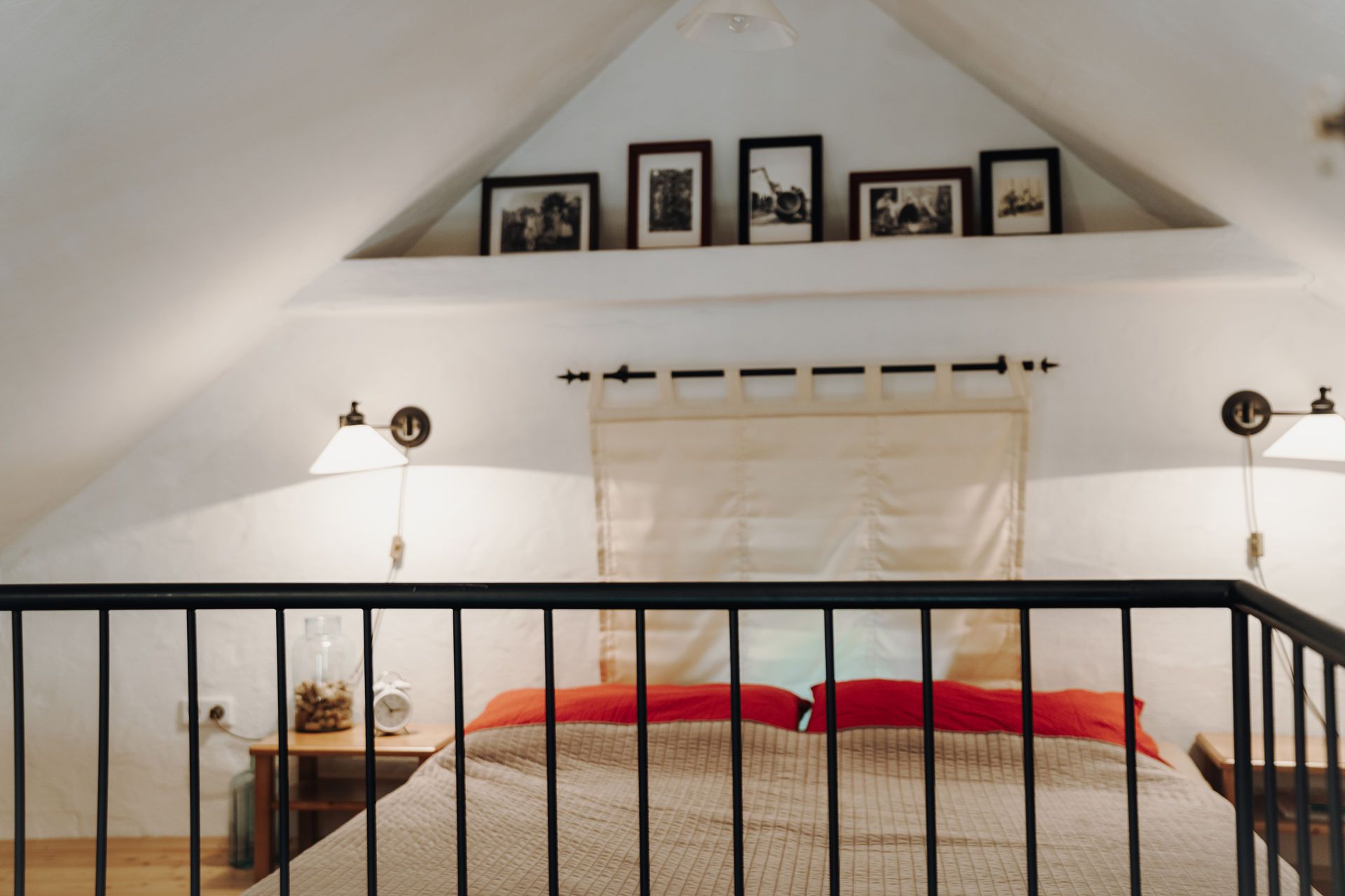 Attic room with double bed, red pillows and wall lamps.