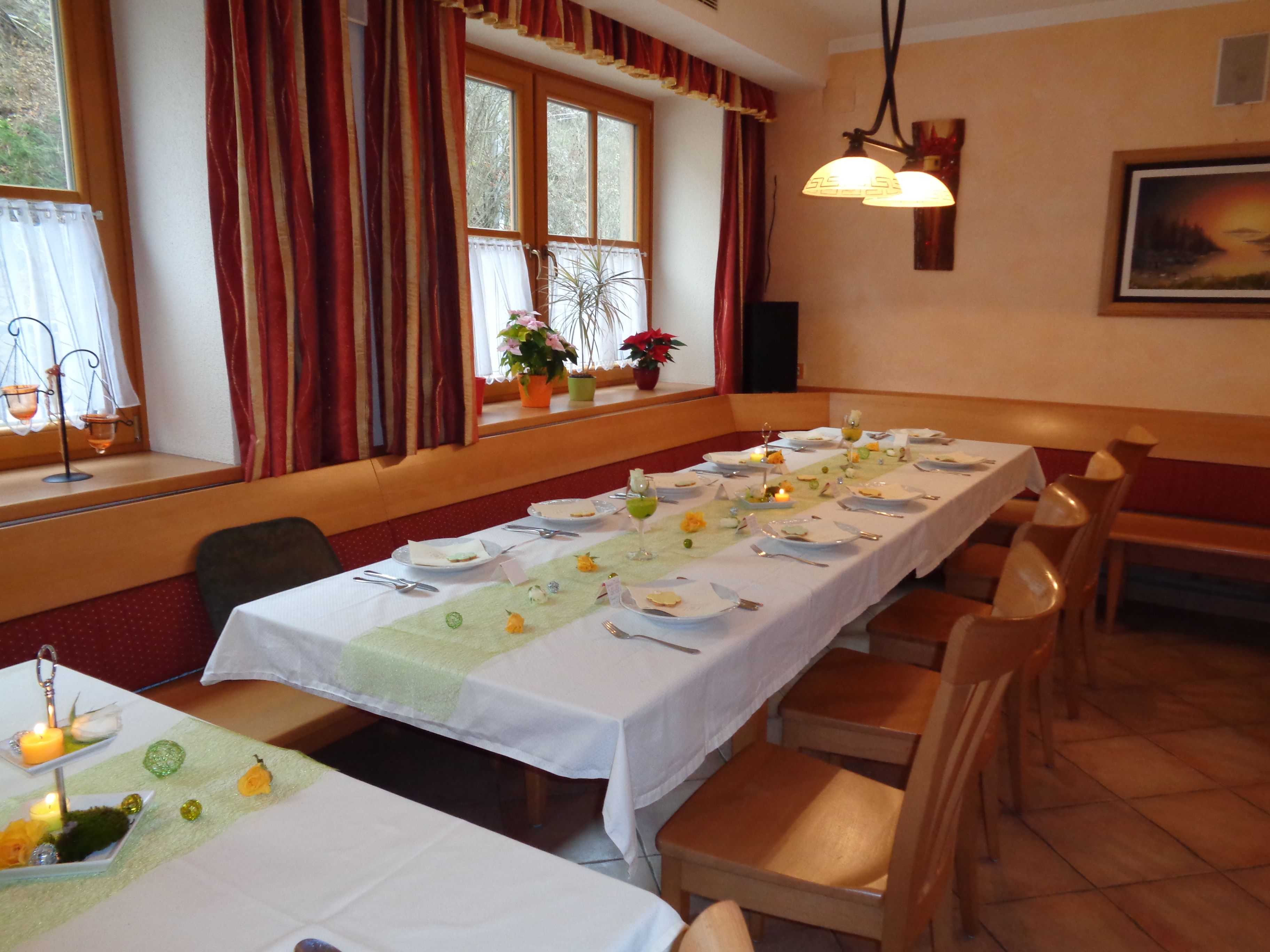 A festively laid table in an inn with white tablecloths, candles and flowers. Wooden furniture and windows with curtains in the background.