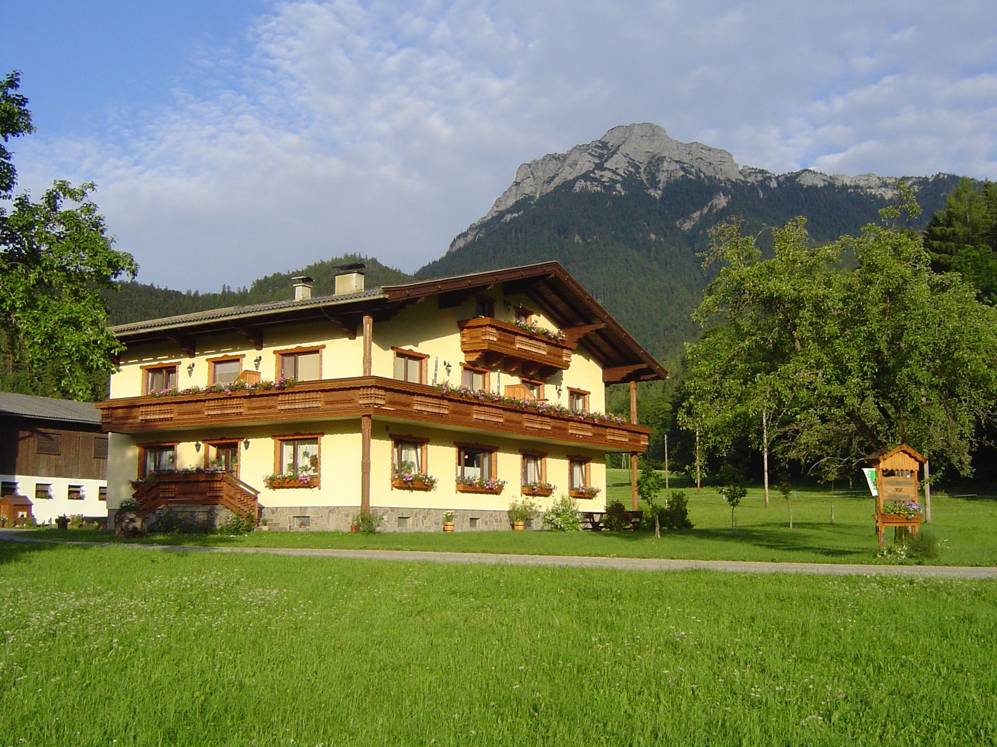 A traditional farmhouse in front of a mountain in a green landscape.
