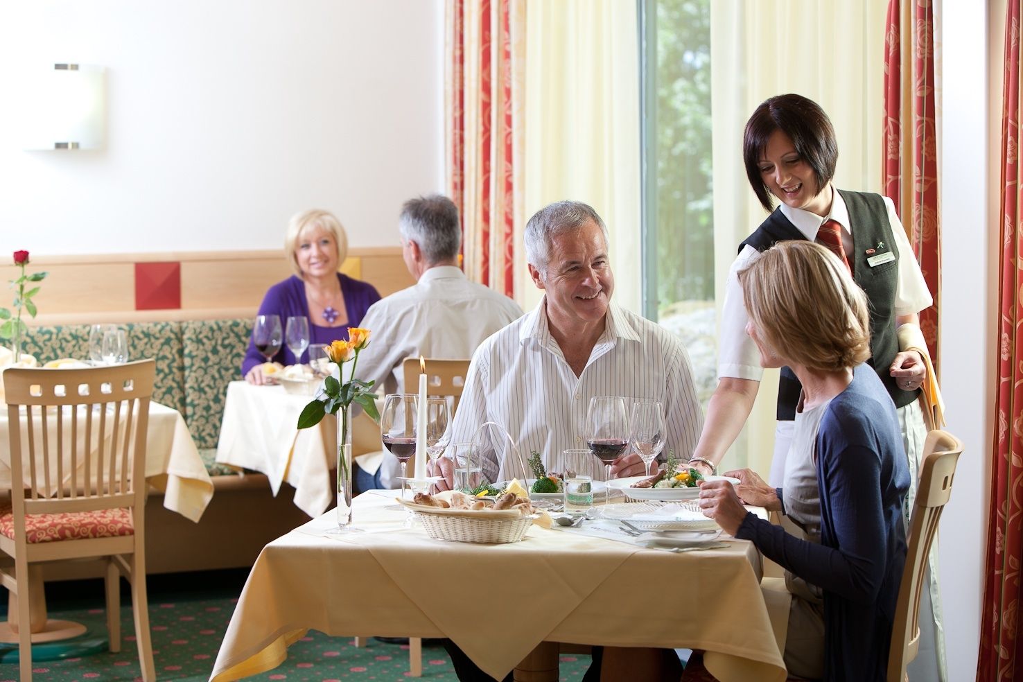 A restaurant with guests sitting at tables and being served by a waitress.