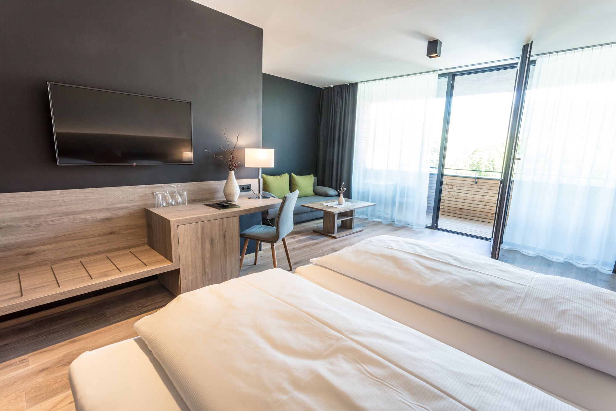 Modern hotel room with double bed, desk, TV and balcony.