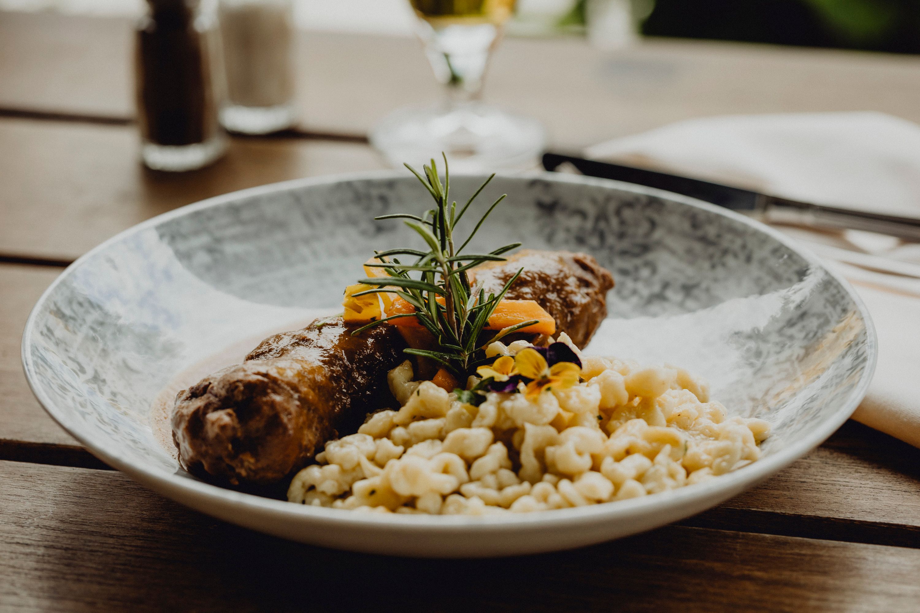 A plate of beef roulade, spaetzle and vegetables, garnished with rosemary and edible flowers.