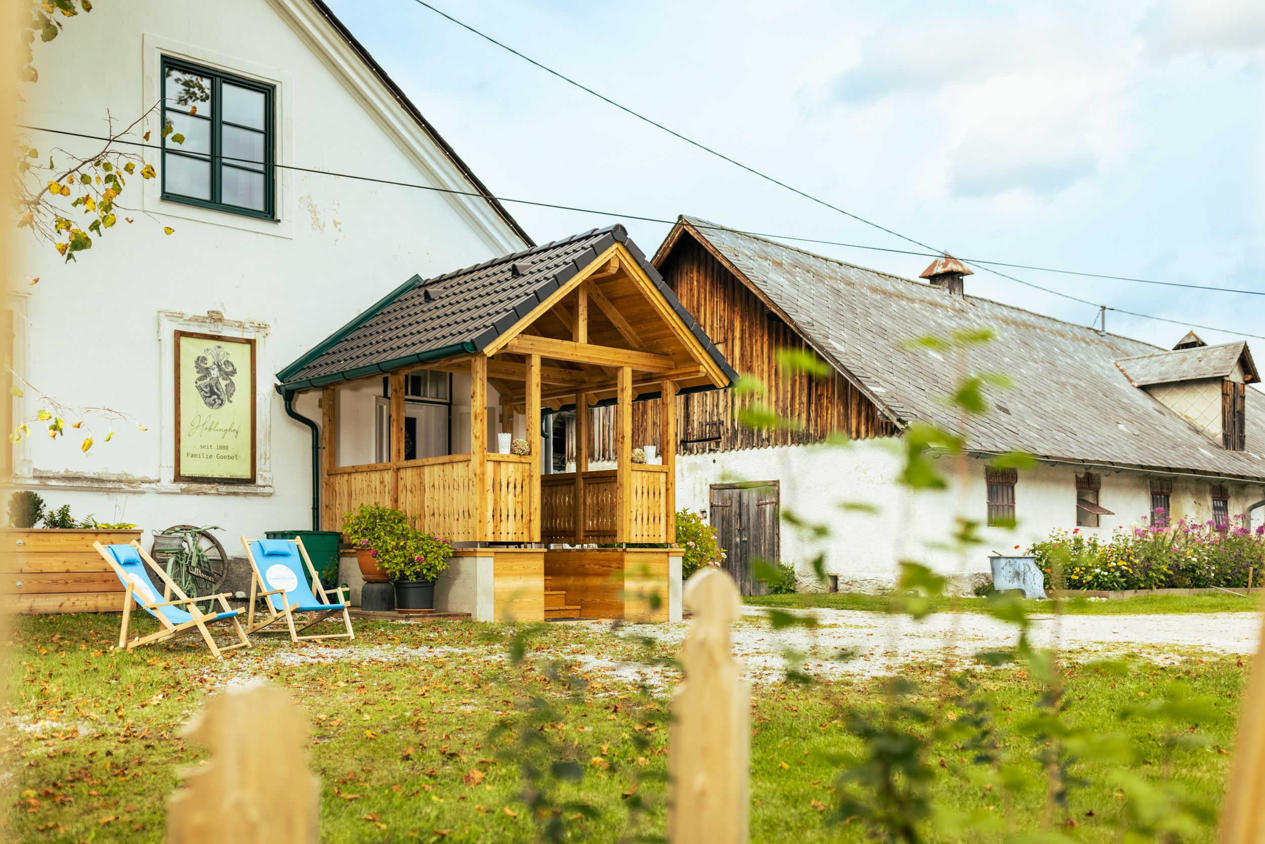 A traditional farmhouse with a wooden balcony and sun loungers in the garden.
