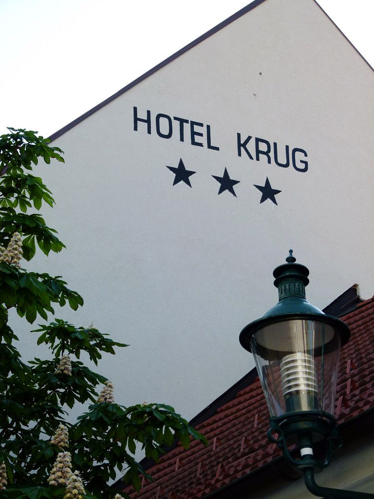 Facade of the Hotel Krug with three stars, tree and street lamp.