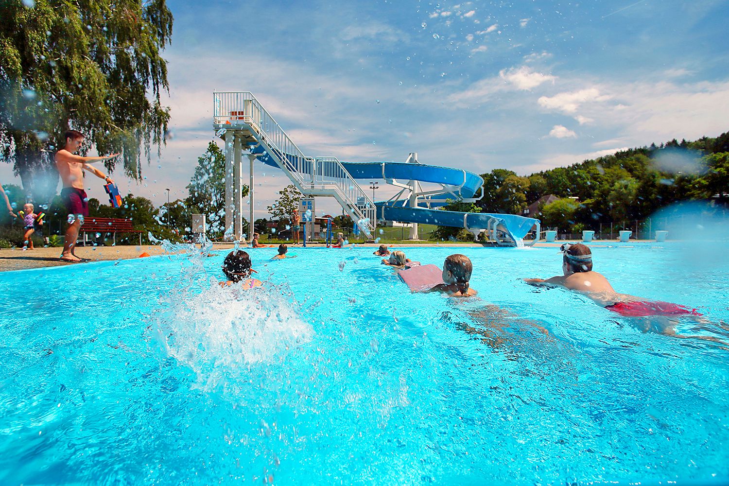 Children swimming in the Neuhofen an der Ybbs outdoor pool with a large water slide in the background.