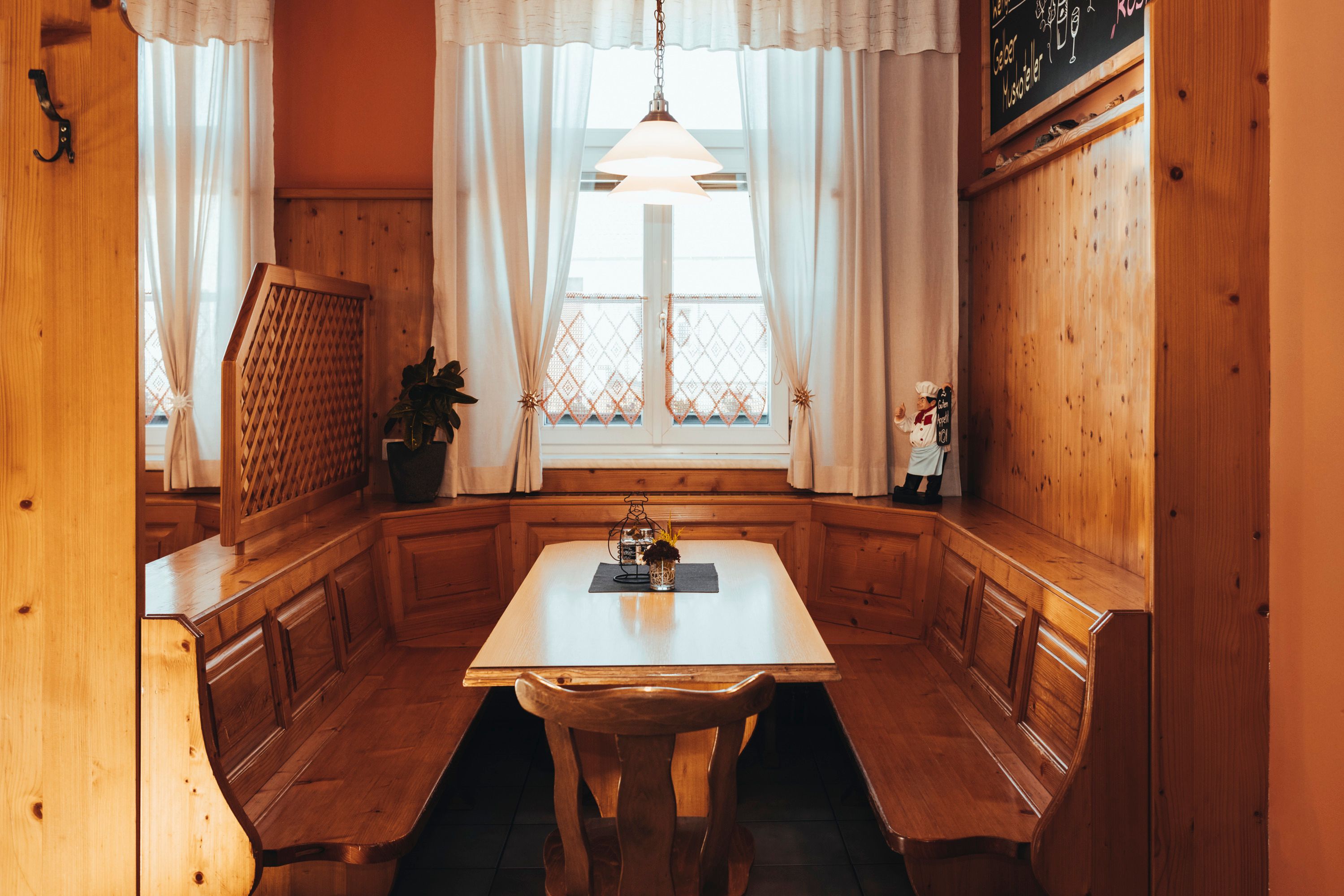 Cozy wooden corner bench with table in a rustic room, decorated with curtains and a small figure.