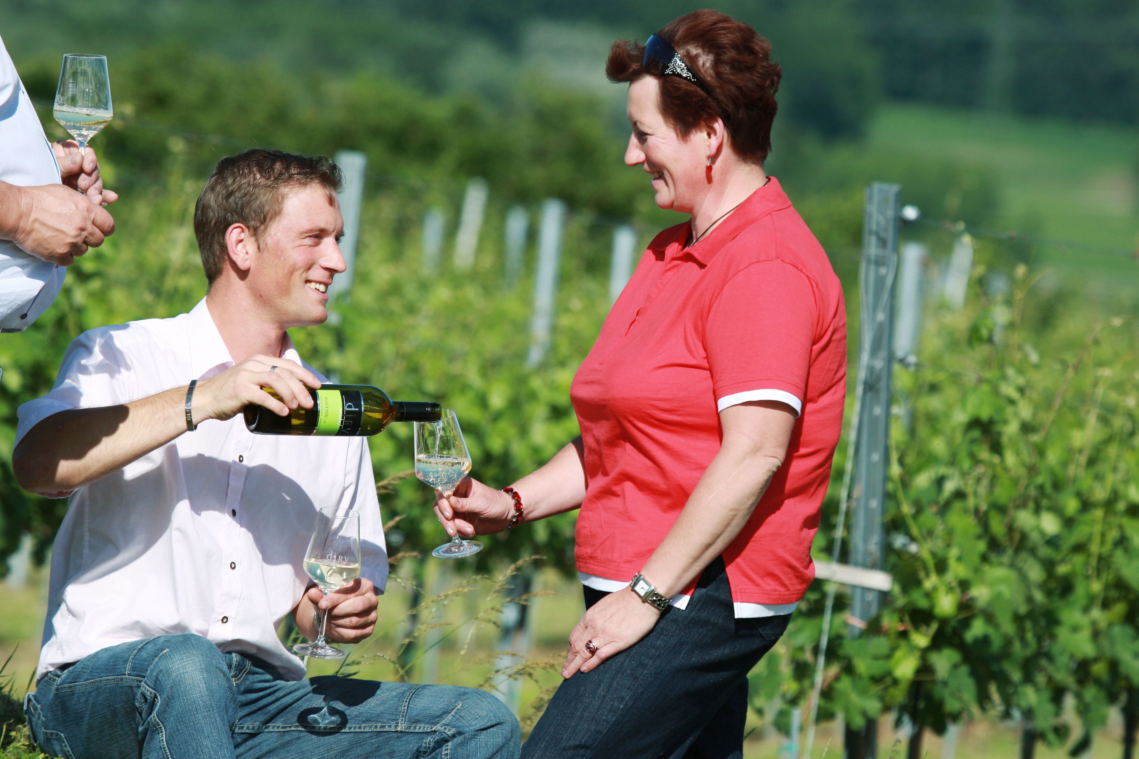 A man pours wine for a woman in a vineyard.