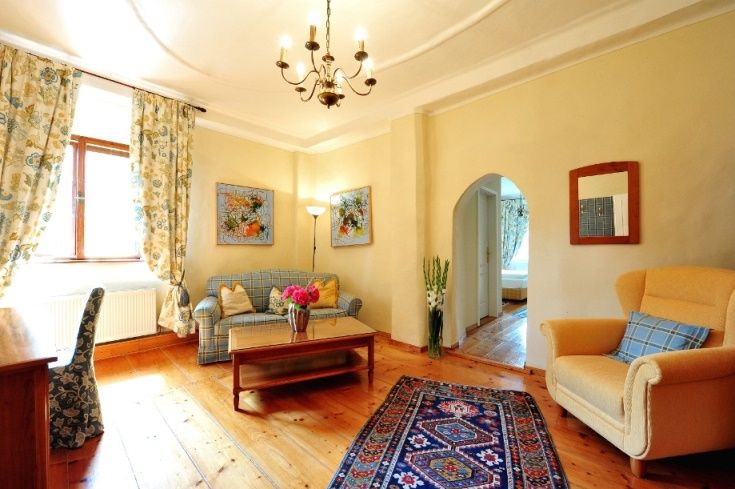 Cozy living room with wooden floor, sofa, armchair, carpet and flowers.