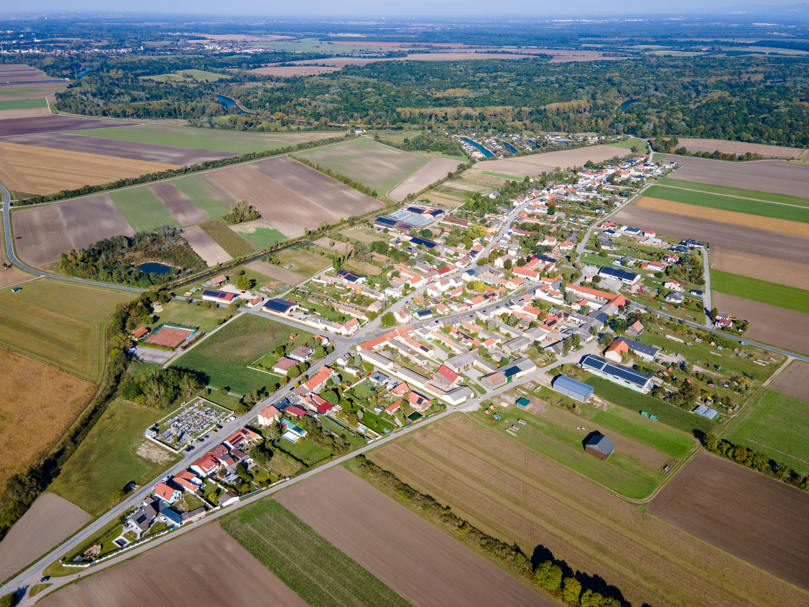 Aerial view of the town of Weiden an der March, showing fields, residential buildings, and the river in the background.