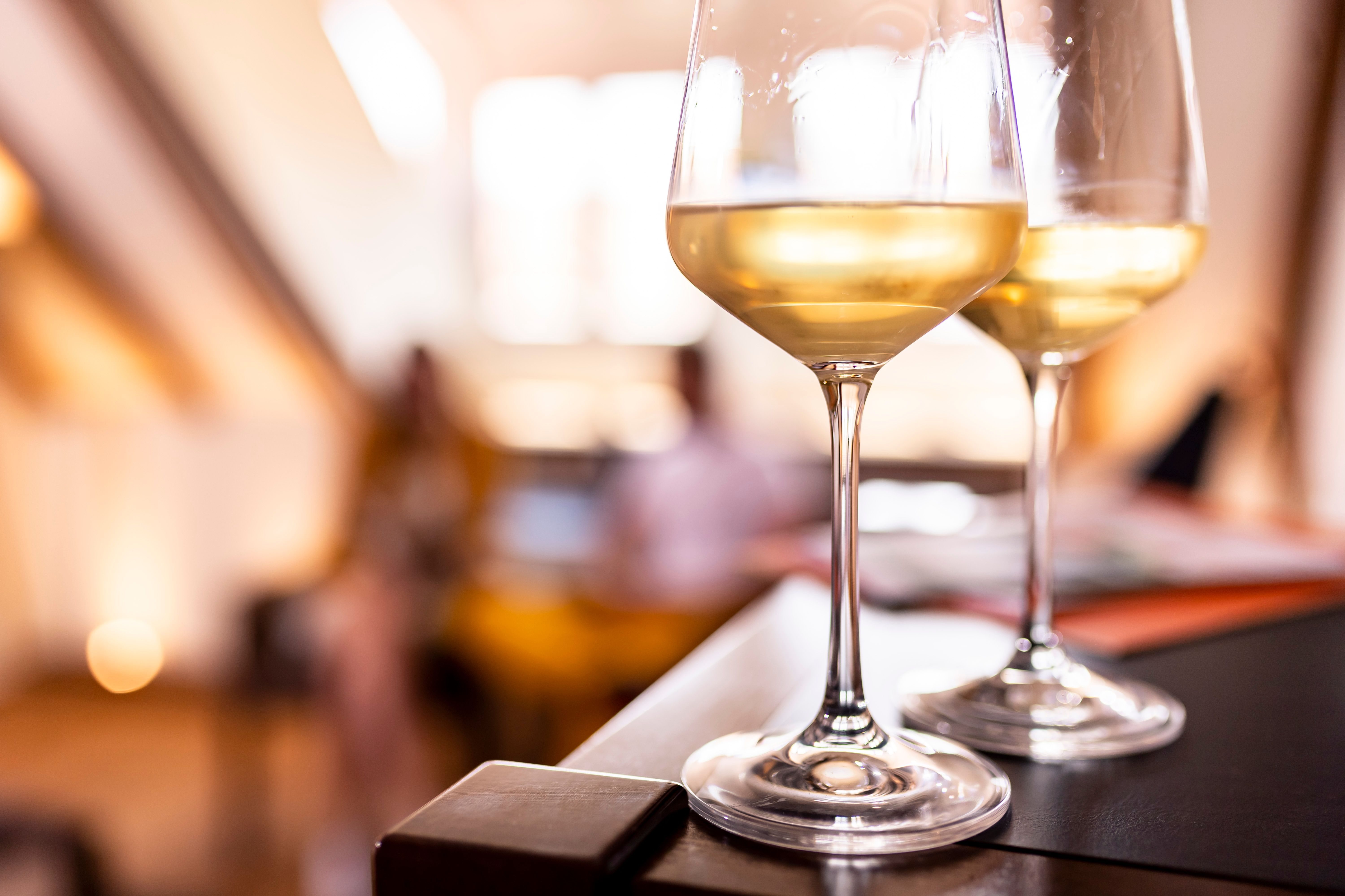 Two glasses of white wine on a table, blurred background with warm light.