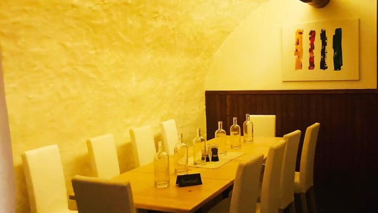 A long table with white chairs in a vaulted cellar, decorated with empty bottles and a modern painting on the wall.