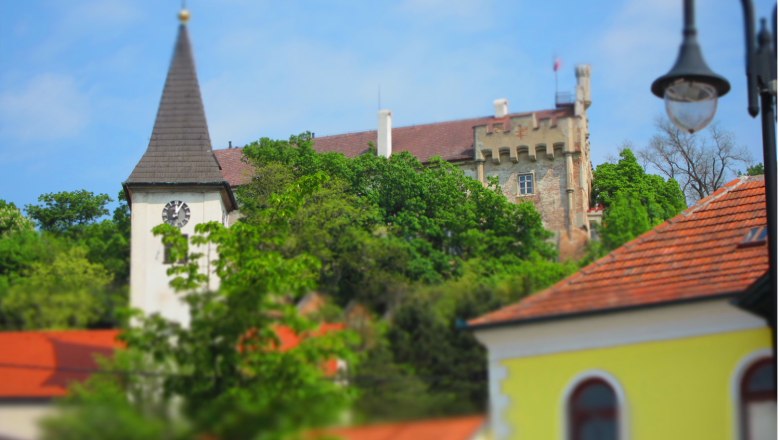 Church tower and castle behind trees, blue sky.