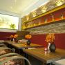 Interior view of a stylish day bar with wooden tables, red benches and decorative flower vases.