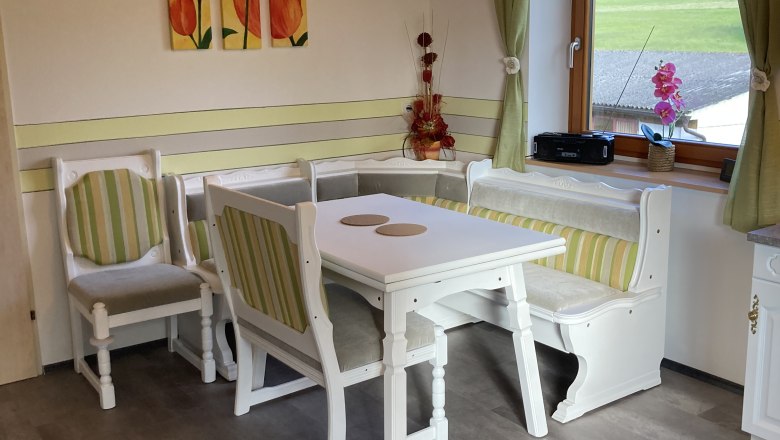 Cozy dining area with wooden furniture and green and white striped upholstery, window with a view of the greenery, tulip picture on the wall.
