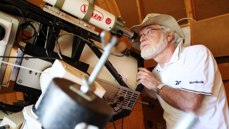 A man with a hat looks through a telescope in an observatory.