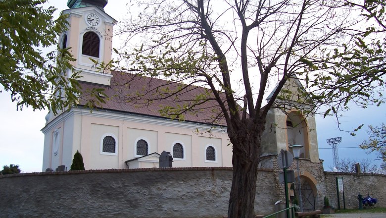 Church with tower and clock, surrounded by trees and a stone wall.