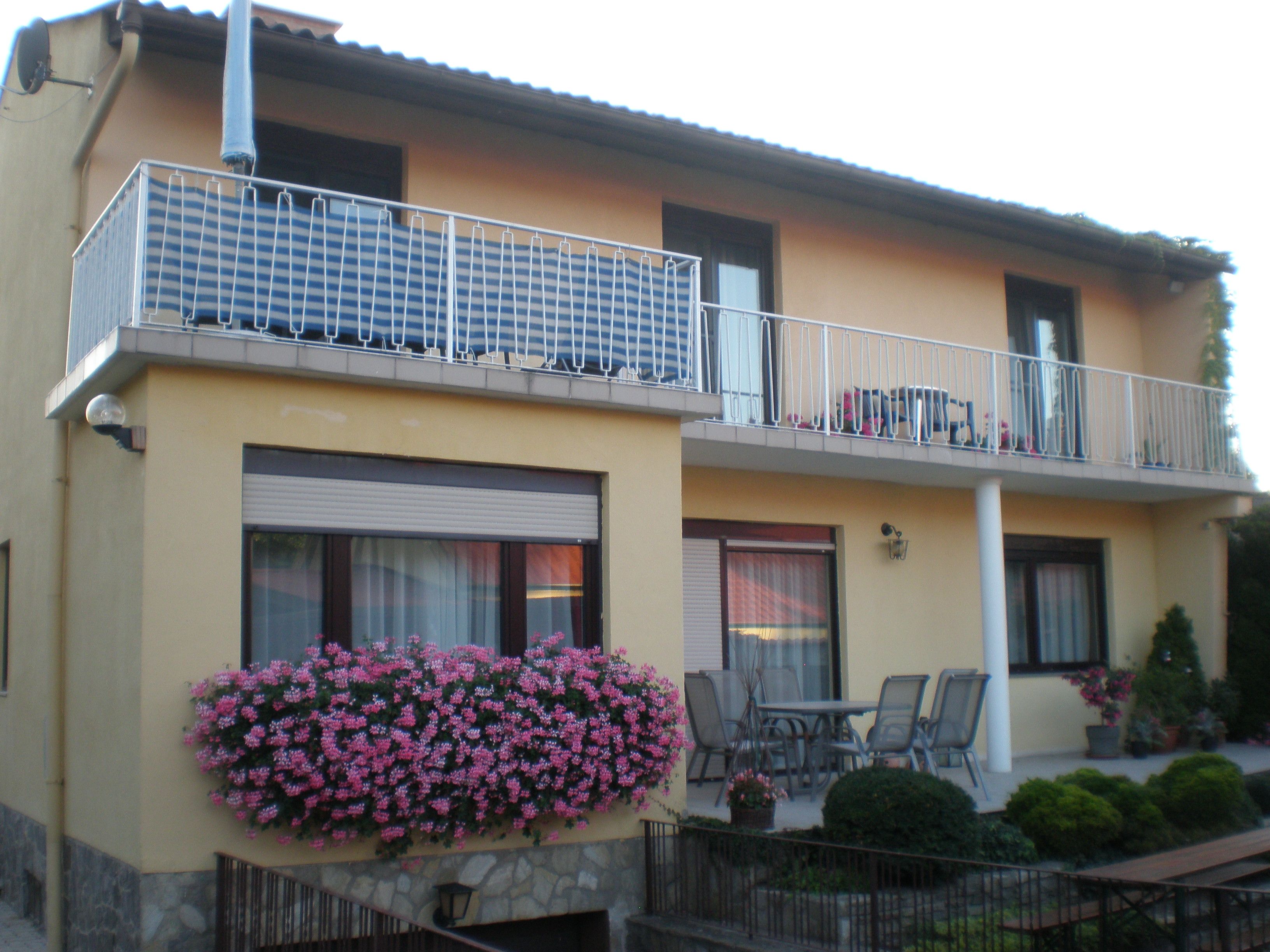 Two-storey house with balcony, flowers and garden furniture.