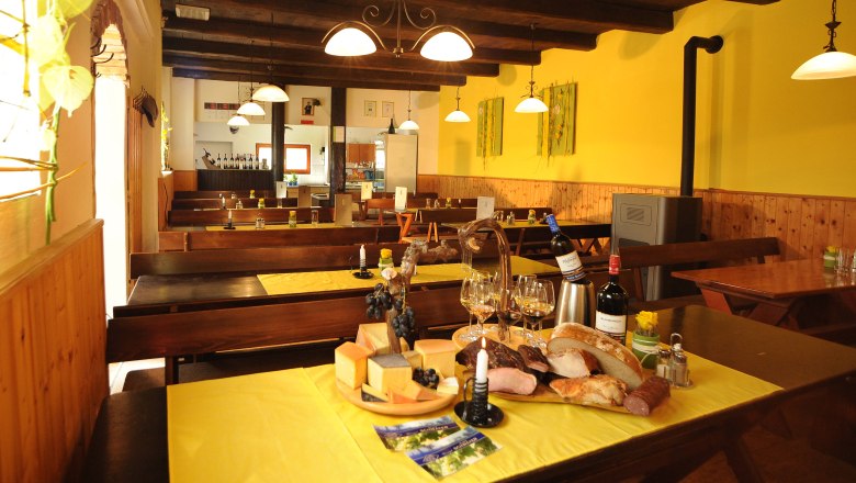 Interior view of a cozy wine tavern with wooden tables, yellow tablecloths and a selection of cheese, bread and wine on a table.