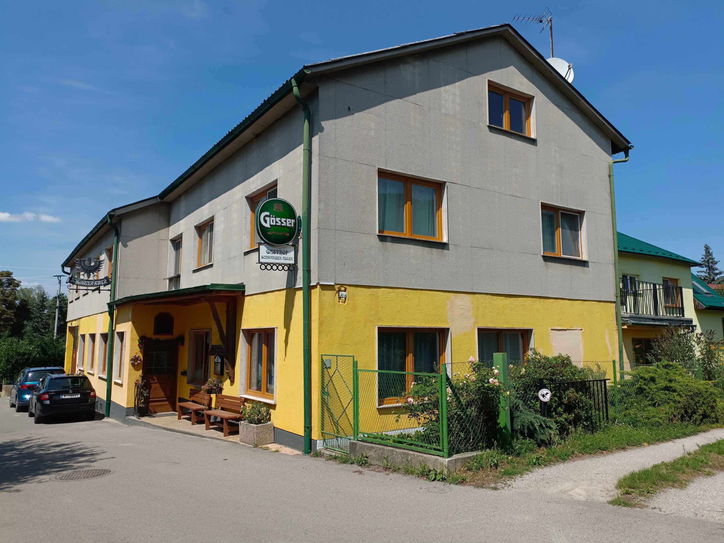 Exterior view of a yellow-grey inn with Gösser sign and parked cars.