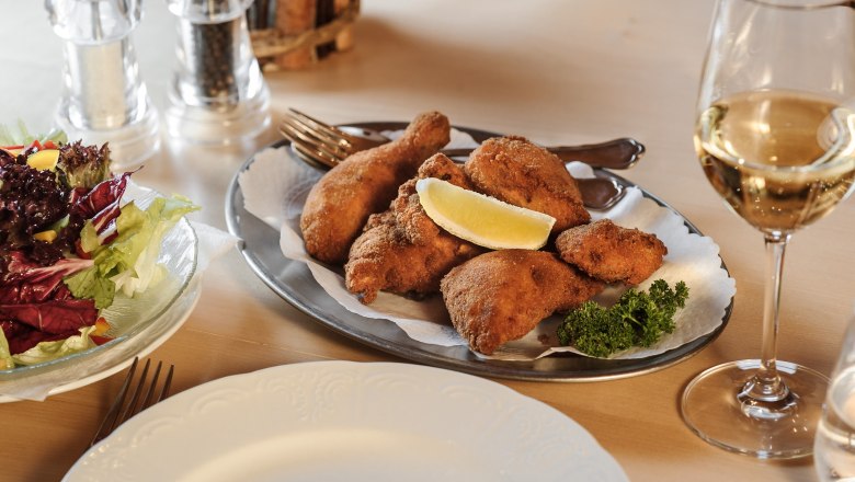 A plate of breaded chicken, salad and a glass of white wine on a table.