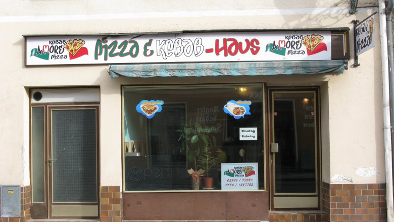 Facade of a pizza and kebab restaurant with signs and windows.