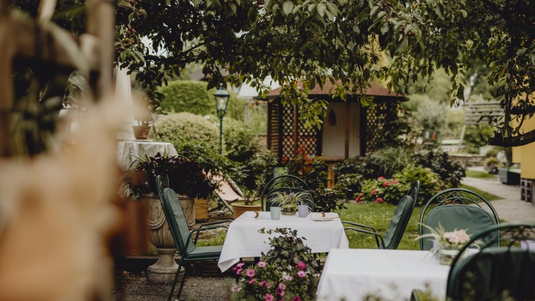 An idyllic garden with laid tables and green chairs under the trees.