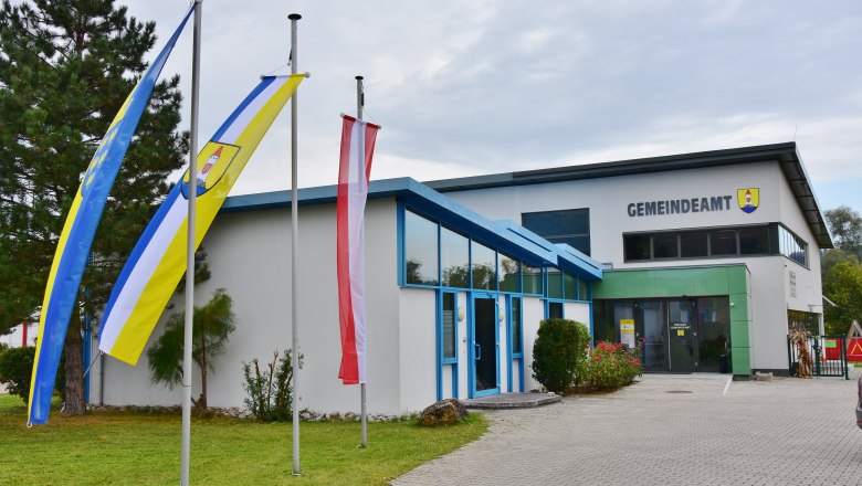 A modern building with the inscription 'Gemeindeamt' and three flagpoles in front of it.