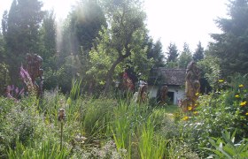 A lush garden with sculptures, trees and a small building in the background.