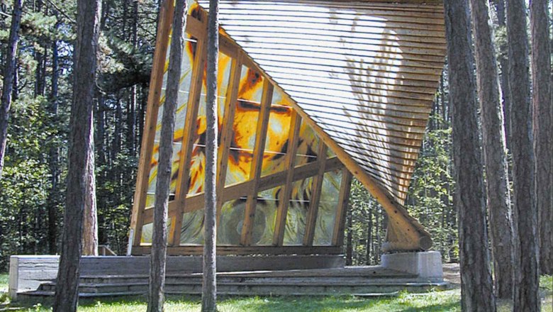 Modern wooden building in the forest with slanted glass windows.