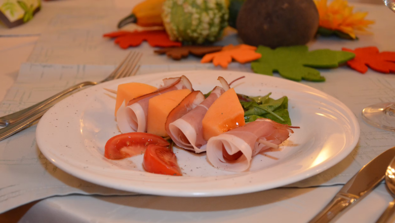 A plate of ham and melon, decorated with tomatoes and salad, on a table with autumnal decorations.