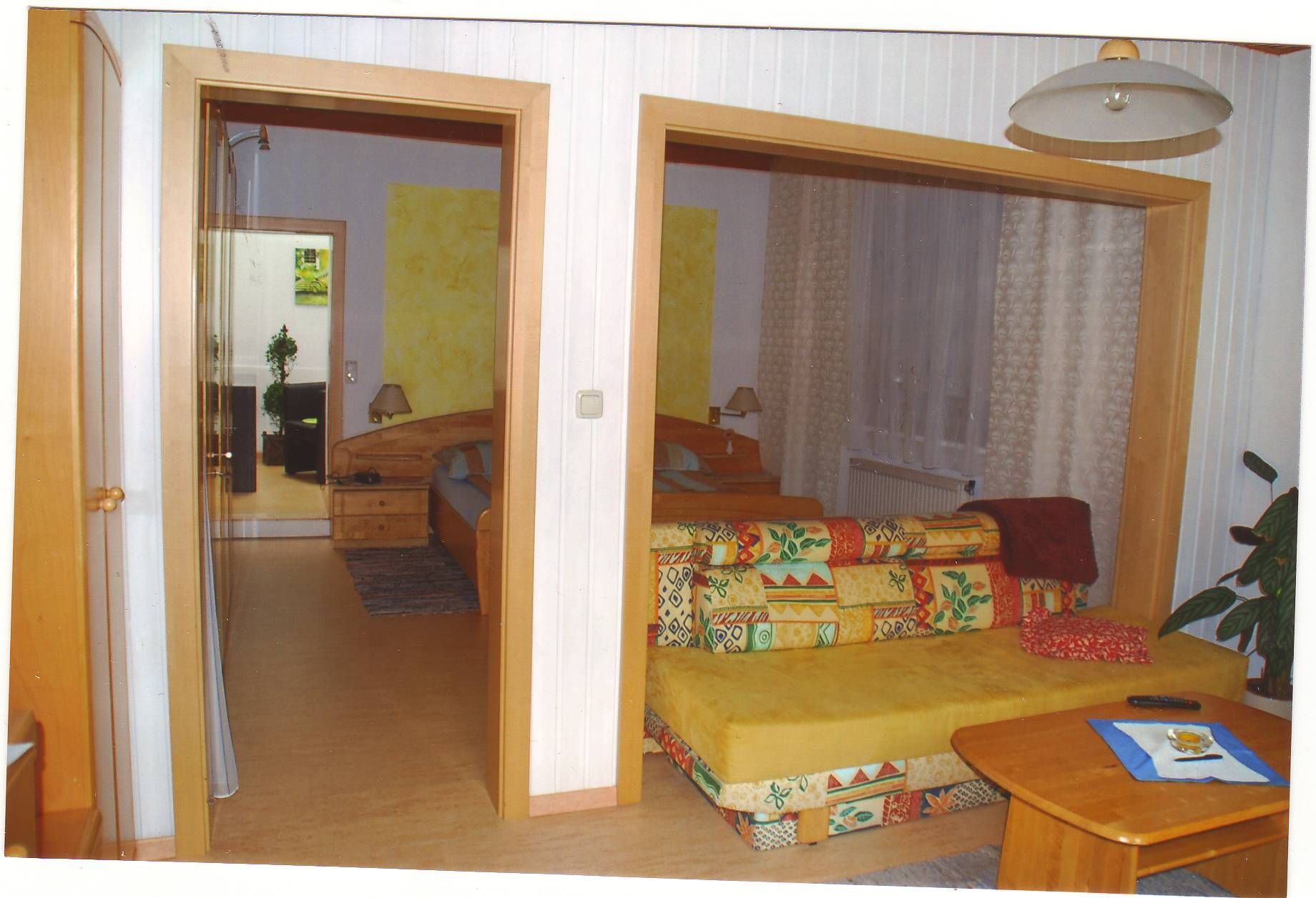 A cozy guest room with a colorful sofa, wooden table and a view of a bedroom with a double bed.